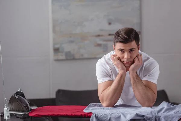 Schöner Mann, das Kinn auf Händen liegend und im Wohnzimmer in die Kamera blickend — Stockfoto