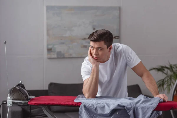 Handsome man resting chin on hand and looking away in living room — Stock Photo