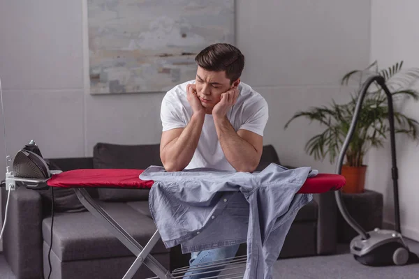 Man resting chin on hands and looking at iron in living room — Stock Photo