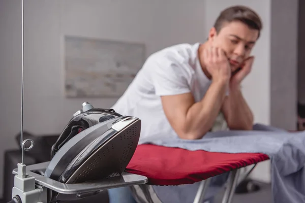 Handsome man resting chin on hands and looking at iron in living room — Stock Photo