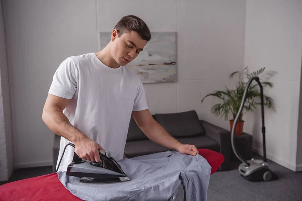 Schöner Mann bügelt Hemd auf Bügelbrett im Wohnzimmer — Stockfoto