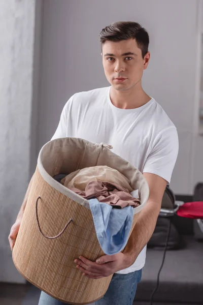 Handsome man holding basket with laundry and looking at camera — Stock Photo