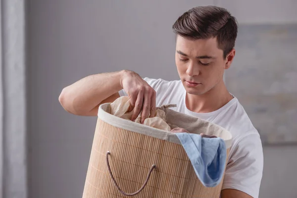 Homem bonito olhando para cesta com lavanderia — Fotografia de Stock