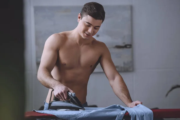 Sexy shirtless man ironing shirt on ironing board — Stock Photo