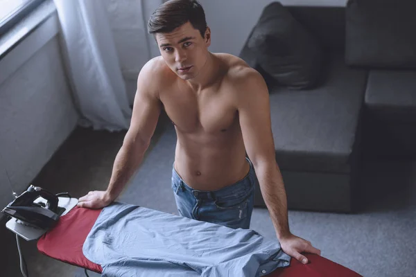 Высокий угол зрения сексуальный мужчина без рубашки, стоящий возле гладильной доски — стоковое фото