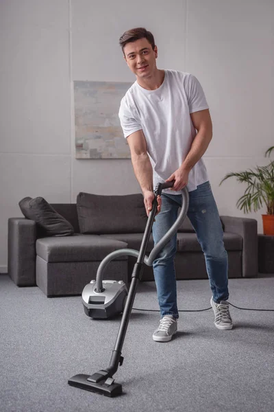Homem bonito limpeza sala de estar com aspirador de pó — Fotografia de Stock
