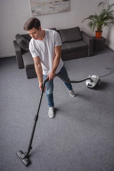 Vista de ángulo alto del hombre guapo sala de estar de limpieza con aspiradora - foto de stock