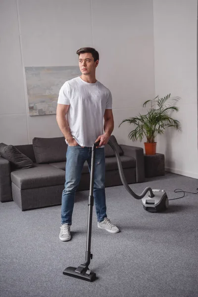 Homem bonito posando com aspirador de pó na sala de estar — Fotografia de Stock