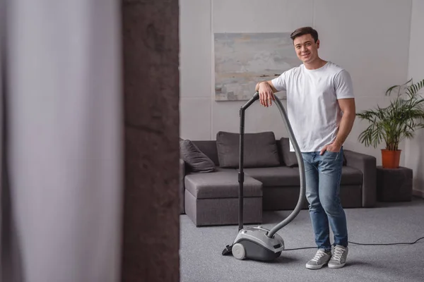 Handsome man leaning on vacuum cleaner in living room — Stock Photo