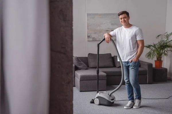 Schöner Mann lehnt an Staubsauger im Wohnzimmer — Stockfoto