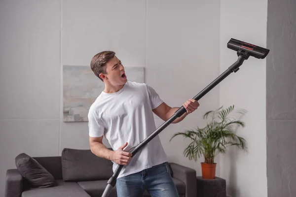 Handsome man having fun with vacuum cleaner in living room — Stock Photo