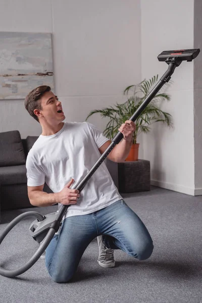 Handsome man having fun with vacuum cleaner in living room — Stock Photo