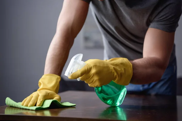 Abgeschnittenes Bild eines Mannes, der Tisch im Wohnzimmer mit Sprühflasche und Lappen reinigt — Stockfoto