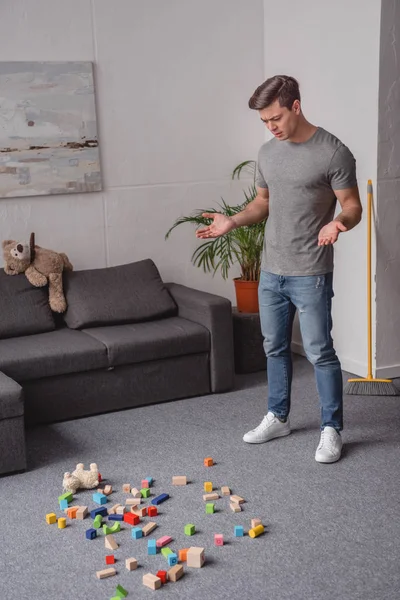 Homme debout dans le salon et regardant des jouets pour enfants dispersés sur le sol — Photo de stock