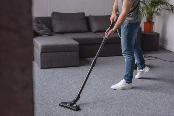 Imagem cortada do homem tapete de limpeza com aspirador de pó na sala de estar — Fotografia de Stock