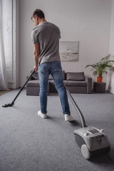 Rückansicht des Mannes, der Teppich mit Staubsauger im Wohnzimmer reinigt — Stockfoto