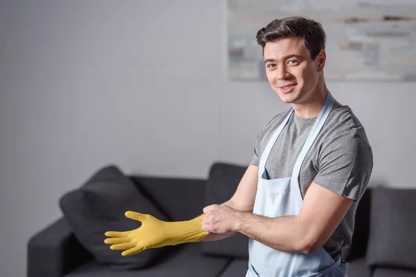 Улыбающийся красивый мужчина в резиновой перчатке для уборки в гостиной — стоковое фото