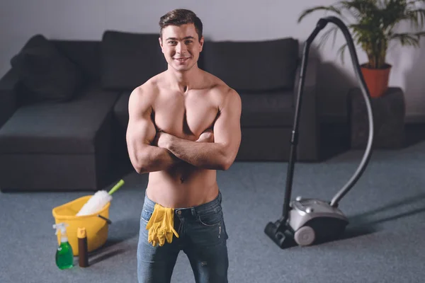 Улыбающийся сексуальный мужчина без рубашки, стоящий со скрещенными руками, резиновые перчатки в джинсах — стоковое фото
