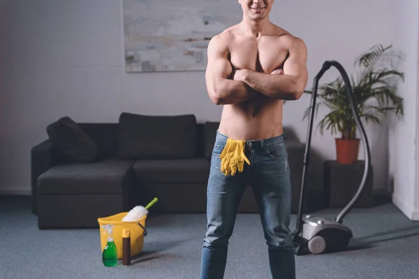 Imagen recortada de hombre sexy sin camisa de pie con los brazos cruzados, guantes de goma en jeans - foto de stock