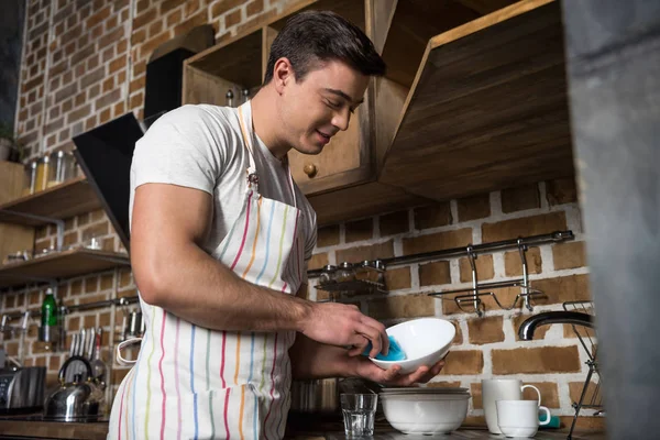 Hombre guapo lavando platos en la cocina - foto de stock