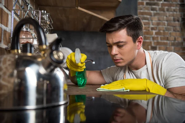 Hombre guapo serio limpieza cocina con aerosol botella y trapo - foto de stock