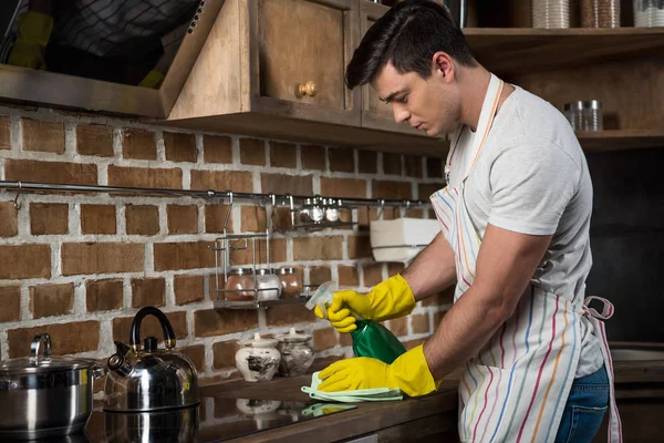 Vue latérale du bel homme qui nettoie la cuisine avec vaporisateur et chiffon — Photo de stock