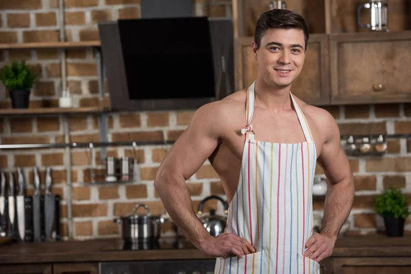 Lächelnd sexy hemdloser Mann steht in Schürze in der Küche — Stockfoto