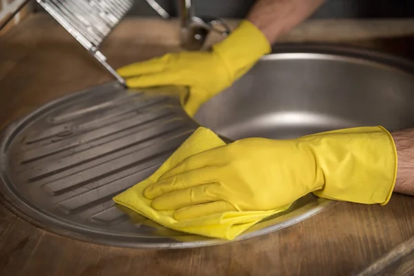 Обрезанное изображение человека, чистящего раковину в резиновых перчатках на кухне — стоковое фото
