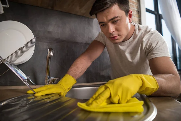 Красивый мужчина моет раковину в резиновых перчатках на кухне — стоковое фото
