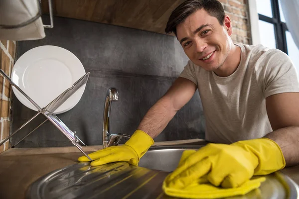 Sorrindo bonito homem limpeza pia na cozinha — Fotografia de Stock