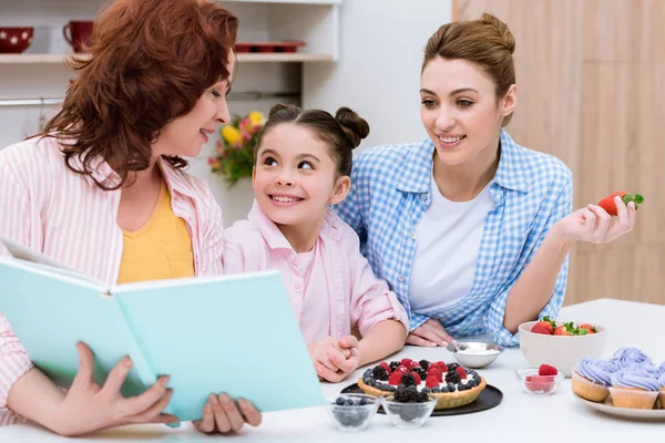 Trois générations de femmes lisant livre de recettes ensemble à la cuisine — Photo de stock