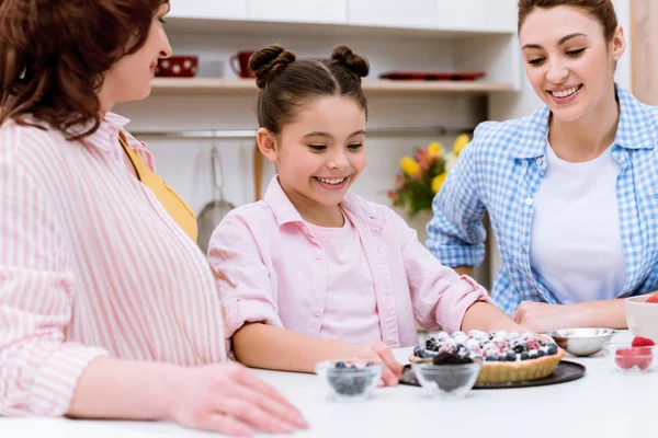 Tres generaciones de mujeres con deliciosa tarta en la cocina - foto de stock