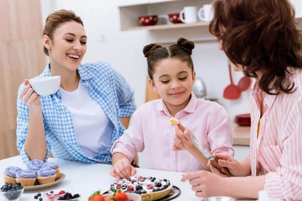 Three generations of beautiful women spending time together on kitchen and eating desserts at kitchen — Stock Photo