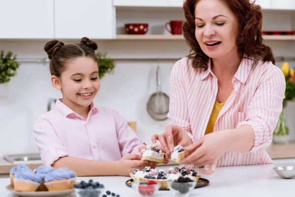 Grandmother and little granddaughter eating delicious tart with berries at kitchen — Stock Photo