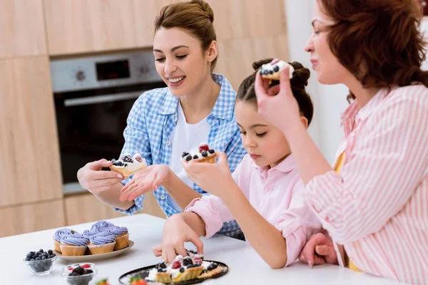 Tres generaciones de mujeres comiendo sabrosa tarta con bayas en la cocina - foto de stock