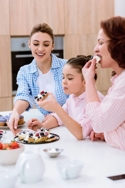 Три поколения женщин едят вкусный пирог с ягодами на кухне — стоковое фото