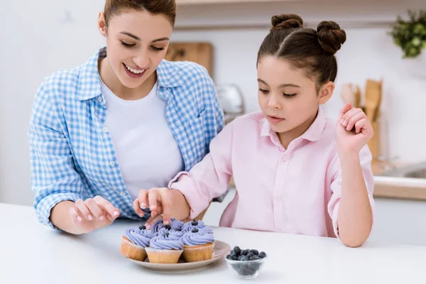 Felice madre e figlia decorare cupcake cremosi con mirtilli — Foto stock