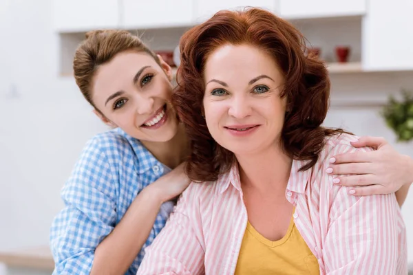 Retrato de cerca de la mujer joven y su madre en la cocina mirando a la cámara - foto de stock