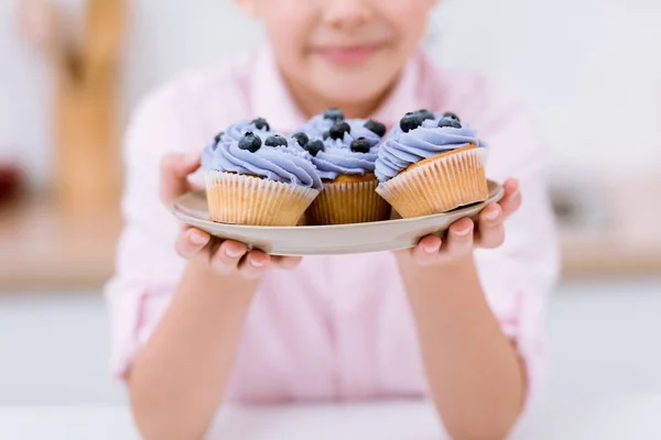 Recortado tiro de niño pequeño sosteniendo placa con cupcakes de arándanos - foto de stock
