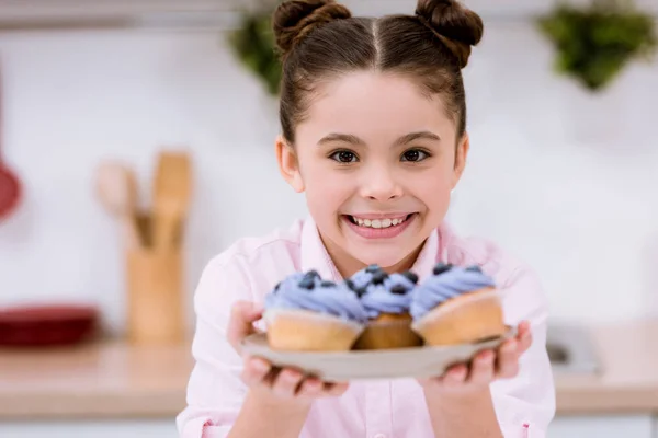 Entzückendes kleines Kind hält Teller mit Blaubeer-Cupcakes — Stockfoto