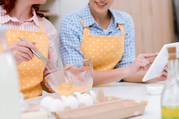 Corte tiro de mulher e sua mãe usando tablet juntos enquanto cozinha na cozinha — Fotografia de Stock