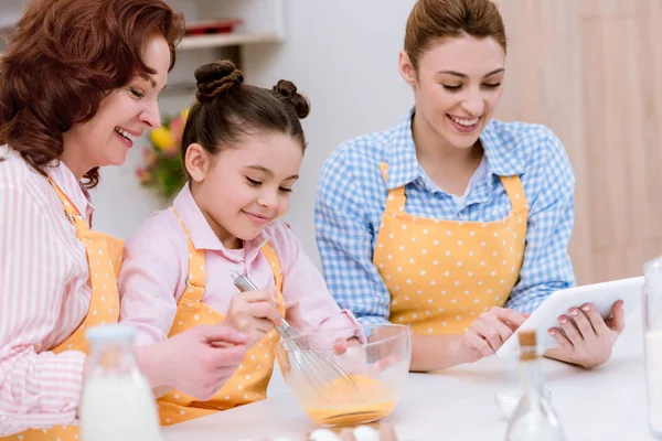 Tres generaciones de mujeres felices en delantales preparando masa juntos en la cocina - foto de stock