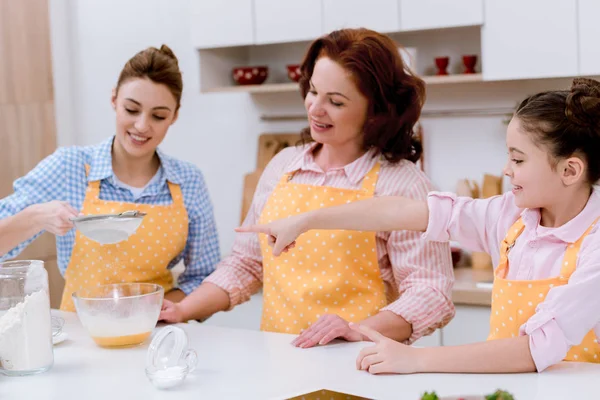 Tres generaciones de mujeres felices preparando la masa juntos en la cocina - foto de stock