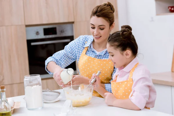 Красивая молодая мать и дочь наливают молоко в миску для теста на кухне — стоковое фото