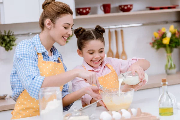 Bela jovem mãe e filha derramando leite em tigela para massa de farinha — Fotografia de Stock