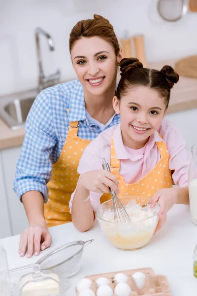 Joven feliz madre e hija mezclando masa para pastelería en la cocina - foto de stock