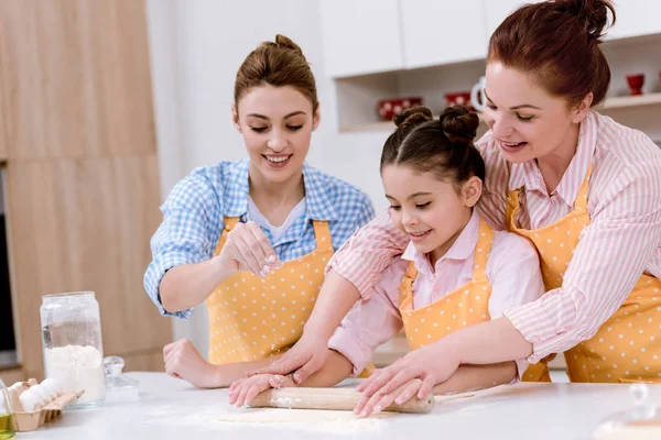 Three generations of beautiful women rolling dough for cookies together at kitchen — Stock Photo