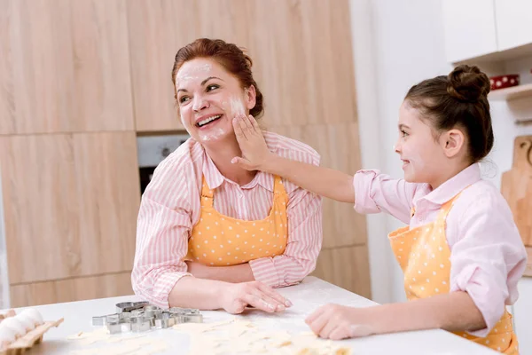 Счастливая бабушка и маленькая внучка играют с мукой на кухне во время приготовления пищи — стоковое фото