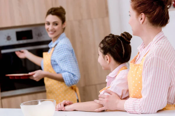 Três gerações de mulheres bonitas em aventais assar pastelaria juntos na cozinha — Fotografia de Stock