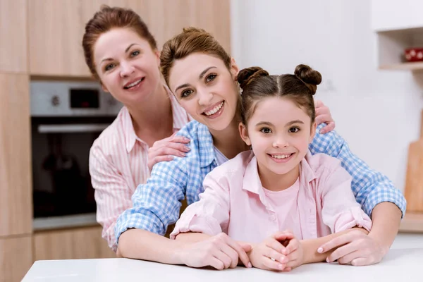 Trois générations de femmes debout en rangée ensemble à la cuisine et regardant la caméra — Photo de stock